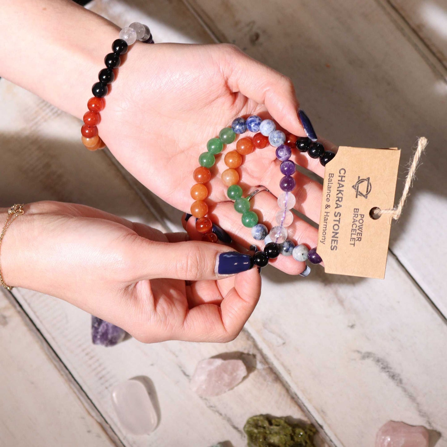 Chakra Power bracelets held by hands with a branded tag on a light wooden surface.