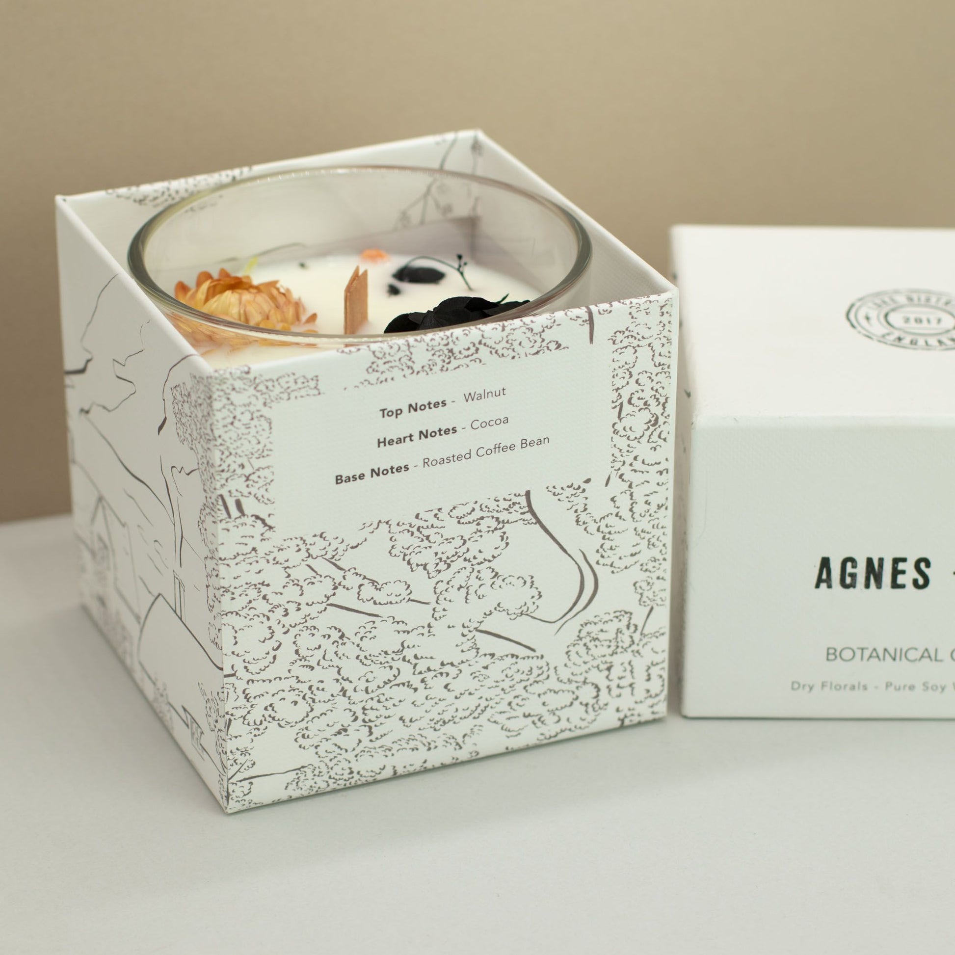 Candle in a decorative box with 'AGNES' branding on a neutral background