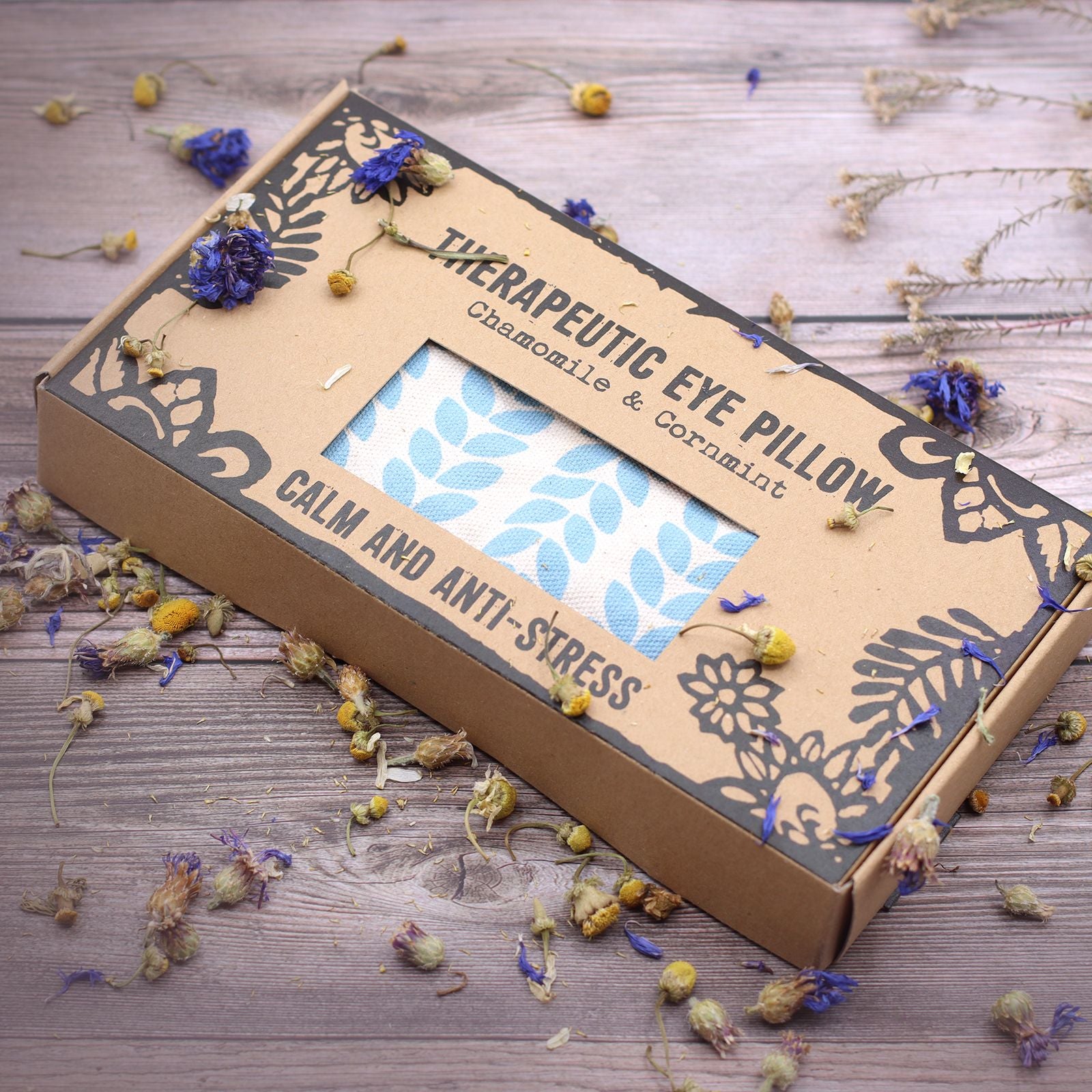Therapeutic eye pillow packaging with chamomile and cornflower on a wooden surface.