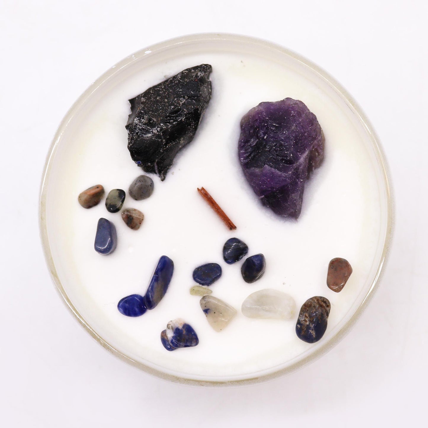 Round white candle with assorted stones and a stick on a white background